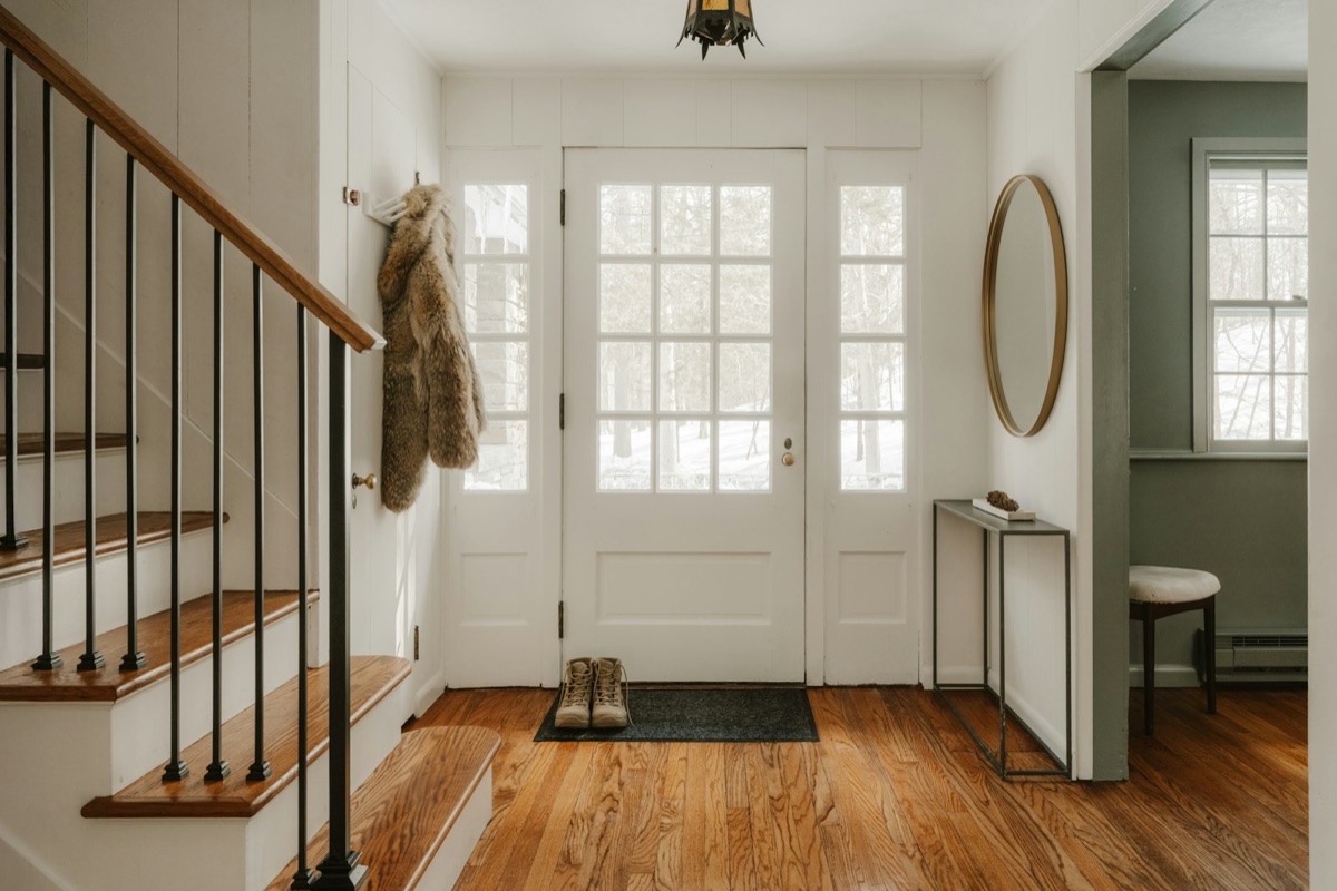 A bright hallway with a glass front door and wooden stairs