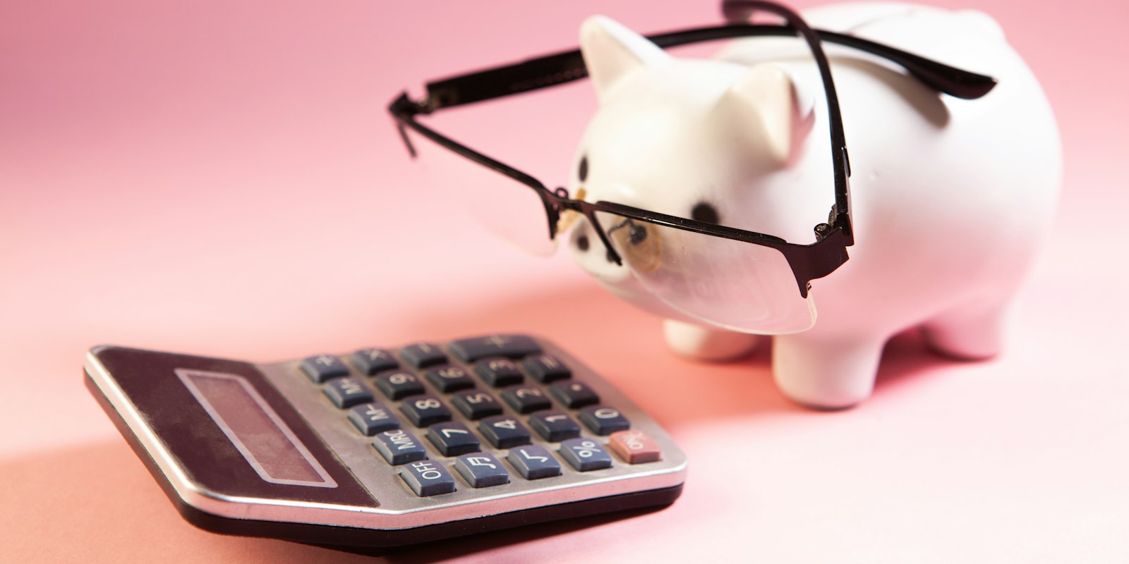 A piggy bank wearing glasses, peering at a calculator